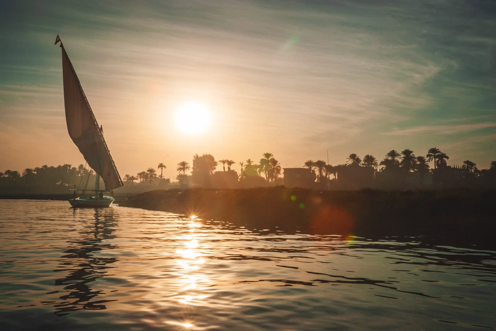 A traditional Egyptian felucca sailing boat on the Nile River at sunset in Aswan, showing the serene and safe side of travel in Upper Egypt.